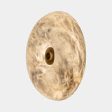 United Alabaster Boutton Wall Light, a round natural alabaster disc with a brass centre button, studio view on grey